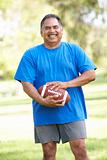 Senior Man Exercising With American Football In Park