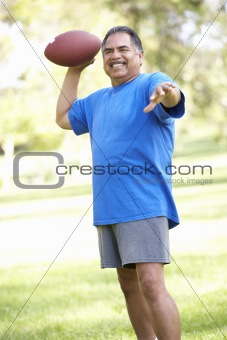Senior Man Exercising With American Football In Park
