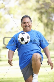 Senior Man Exercising With Football In Park