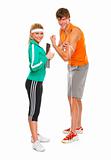 Male athlete measuring biceps and smiling girl in sportswear showing thumbs up
