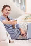 Portrait of a woman having a glass of wine while using her laptop