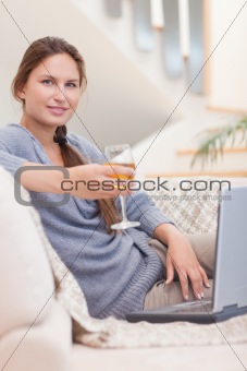 Portrait of a woman having a glass of wine while using her laptop