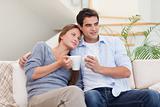 Lovely couple watching TV while drinking coffee