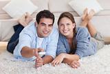 Smiling couple watching TV while lying on a carpet