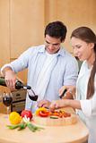 Portrait of a cute man pouring a glass of wine while his wife is cooking