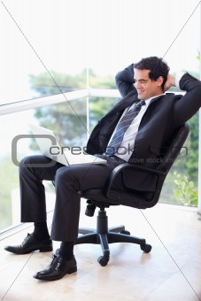 Portrait of a relaxed businessman sitting on an armchair working with a laptop