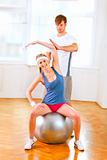 Smiling girl making exercises on fitness ball assisted by her personal trainer 
