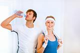 Male athlete drinking water from bottle and smiling girl in sportswear with towel
