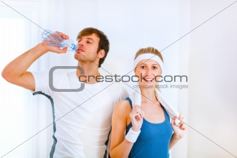 Male athlete drinking water from bottle and smiling girl in sportswear with towel
