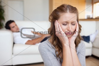 Woman having headache while man lying on sofa behind her
