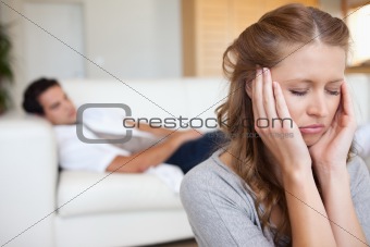 Woman experiencing headache with man on the sofa behind her