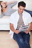 Man reading the news while his girlfriend is listening to music on the sofa