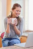 Woman having coffee while looking on her laptop