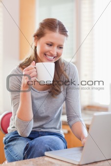 Smiling woman enjoying coffee while typing on her laptop