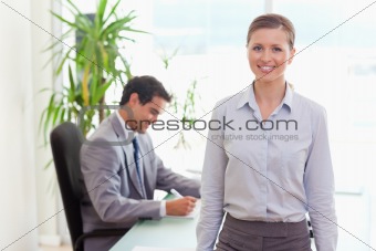 Smiling tradeswoman with colleague sitting behind her