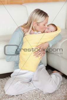 Mom kissing her baby that is wrapped into a cover