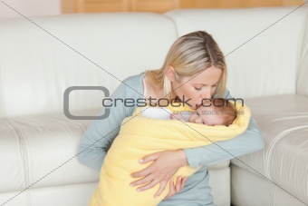 Lovely mother kissing her baby which is wrapped into a cover
