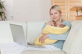 Mother with laptop on the sofa holding her baby