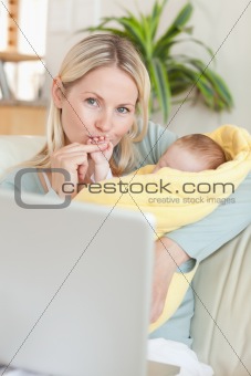 Mother kissing her baby's hand while sitting on the sofa