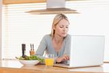 Woman with salad and orange working on laptop in the kitchen