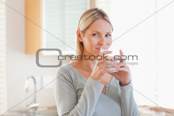 Woman standing in the kitchen drinking some water