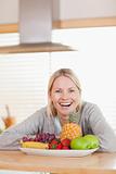 Laughing woman sitting behind plate of fruits