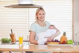 Woman standing in the kitchen while holding her baby