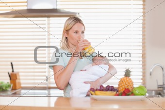 Woman taking a sip of juice while holding her baby