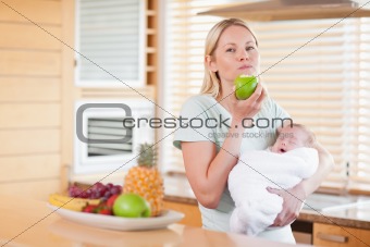 Woman chewing on apple while holding baby on her arms