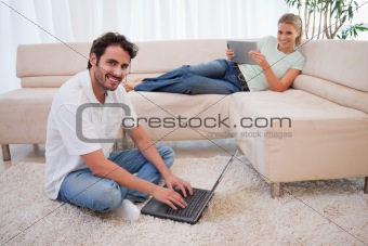 Woman using a tablet computer while her boyfriend is using a notebook