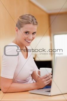 Portrait of a woman using a laptop while drinking a cup of a coffee