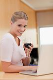 Portrait of a woman using a laptop while drinking red wine