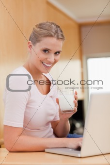 Portrait of a smiling woman using a laptop while drinking milk