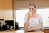 Young woman reading the news while drinking orange juice