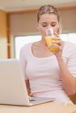 Portrait of a young woman using a laptop while drinking juice