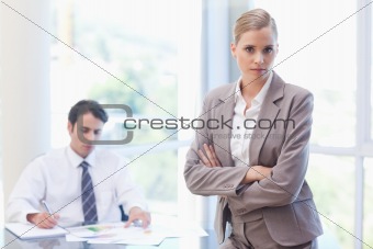 Serious businesswoman posing while her colleague is working