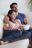 Portrait of a couple watching television while eating popcorn