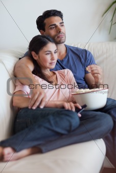 Portrait of a couple watching television while eating popcorn