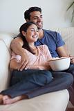 Portrait of a happy couple watching television while eating popcorn