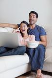 Portrait of a laughing couple watching a movie while eating popcorn