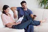 Woman reading a book while her fiance is watching television