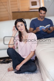 Portrait of a woman listening to music while her husband is reading a book