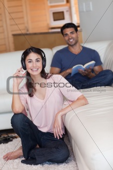 Portrait of a young woman listening to music while her husband is reading a book