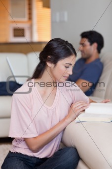 Portrait of a woman reading a book while her husband is using a laptop
