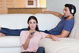 Woman watching television while her boyfriend is listening to music