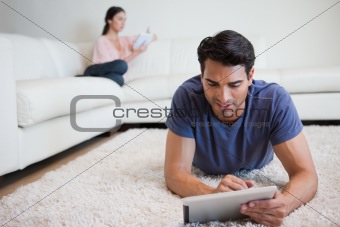 Man using a tablet computer while his girlfriend is reading a book