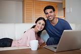 Smiling couple using a laptop while having a tea