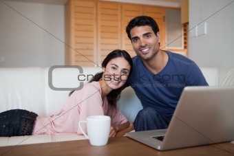 Smiling couple using a laptop while having a tea