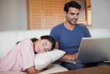 Man using a laptop while his fiance is sleeping