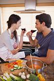 Portrait of a charming couple having a glass of wine while cooking